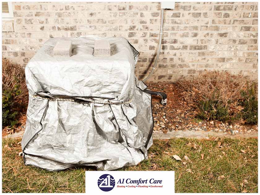 Do You Need to Cover Your Outdoor HVAC Unit This Fall? Outdoor HVAC unit covered with a silver tarp, surrounded by fallen leaves and grass, featuring A-1 Comfort Care logo, illustrating seasonal maintenance advice for homeowners.