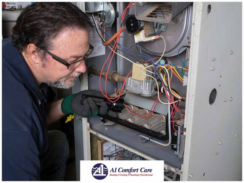HVAC technician inspecting the interior components of a furnace, troubleshooting potential issues related to clicking sounds, with A-1 Comfort Care branding visible.